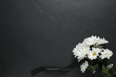 White chrysanthemum flowers and ribbon on black table, top view with space for text. Funeral symbols