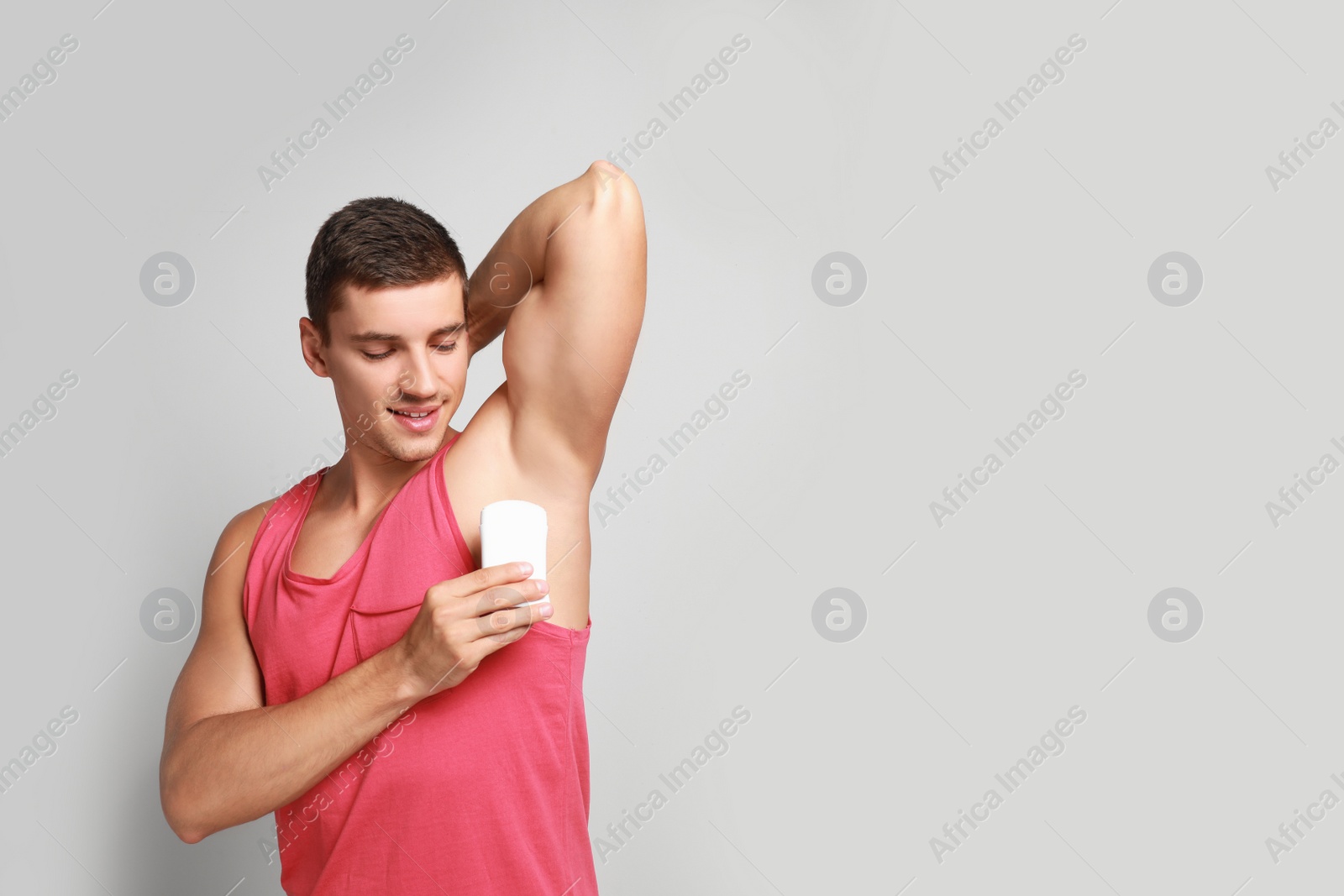 Photo of Young man applying deodorant to armpit on light background. Space for text