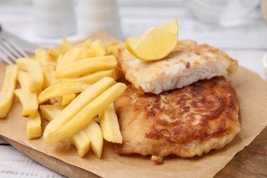 Tasty soda water battered fish, potato chips and lemon slice on white wooden table, closeup