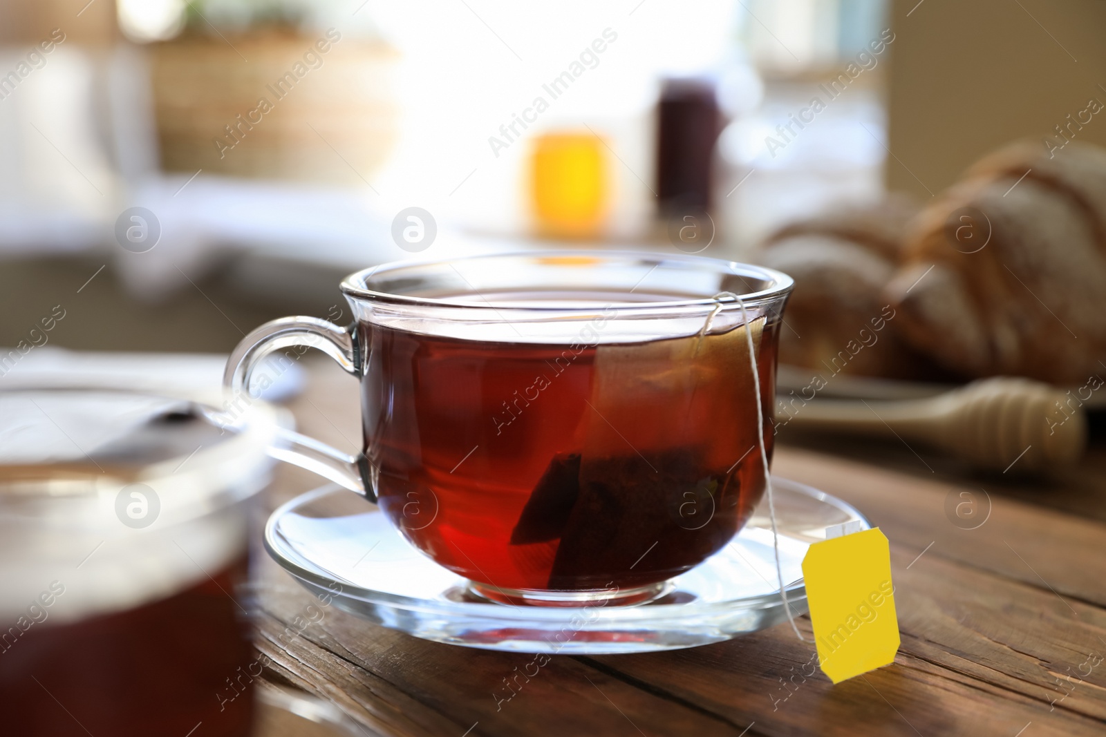 Photo of Tea bag in glass cup on wooden table indoors, closeup