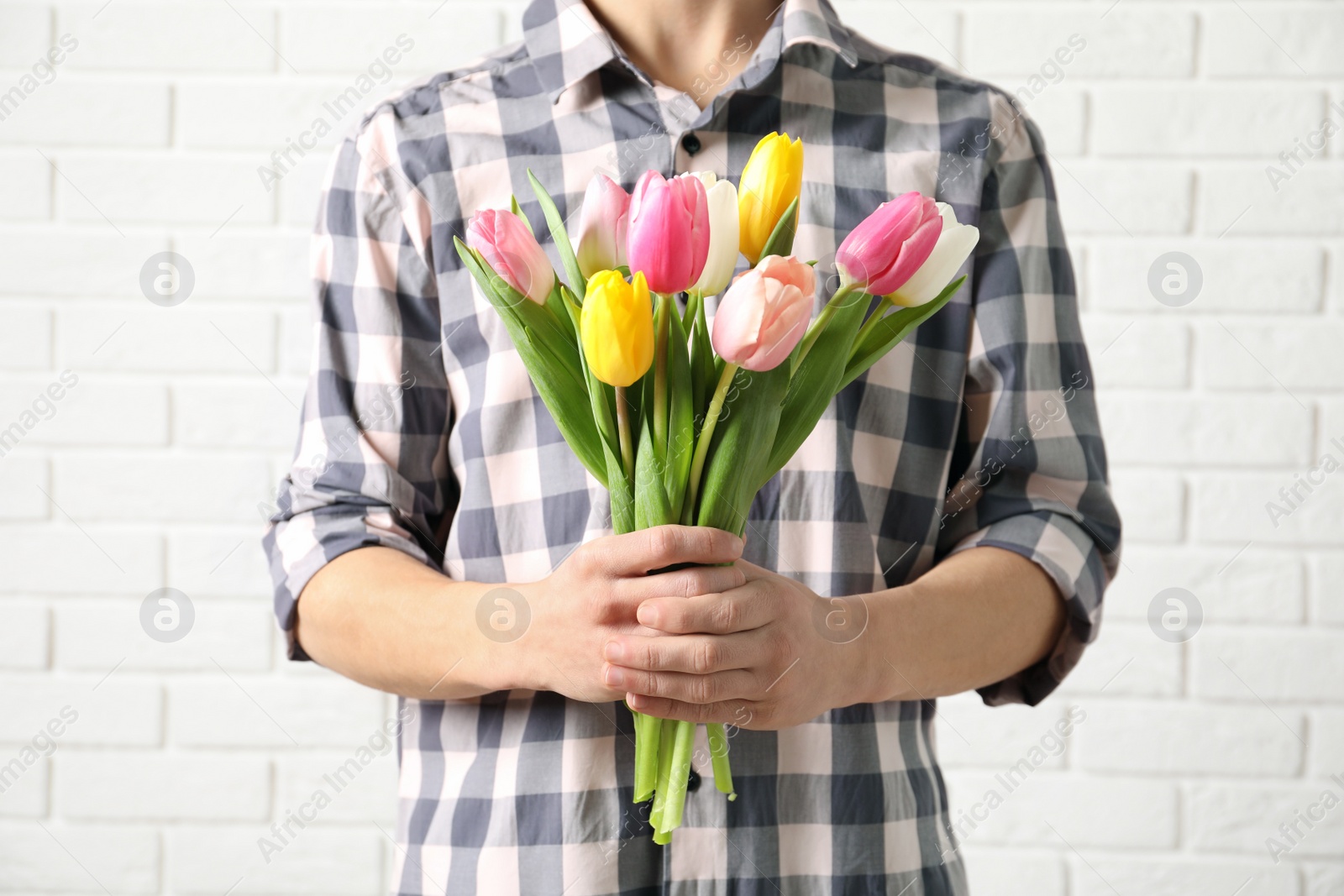 Photo of Man holding bouquet of beautiful spring tulips near brick wall, closeup. International Women's Day