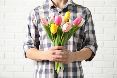 Photo of Man holding bouquet of beautiful spring tulips near brick wall, closeup. International Women's Day