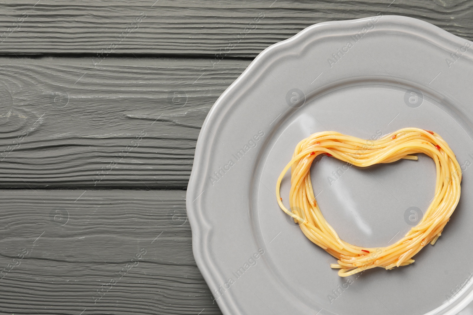 Photo of Heart made with spaghetti on grey wooden table, top view. Space for text