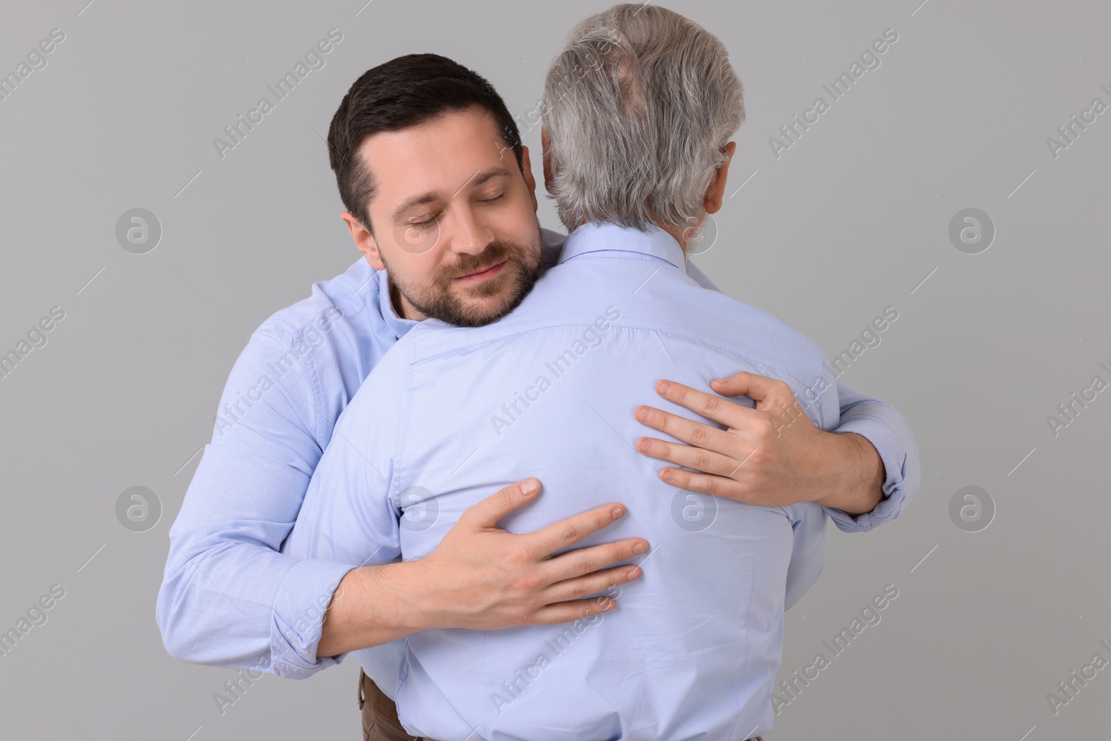 Photo of Happy son and his dad hugging on gray background