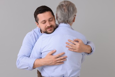 Happy son and his dad hugging on gray background