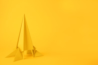 Photo of Origami art. Handmade bright paper rocket on yellow background, space for text