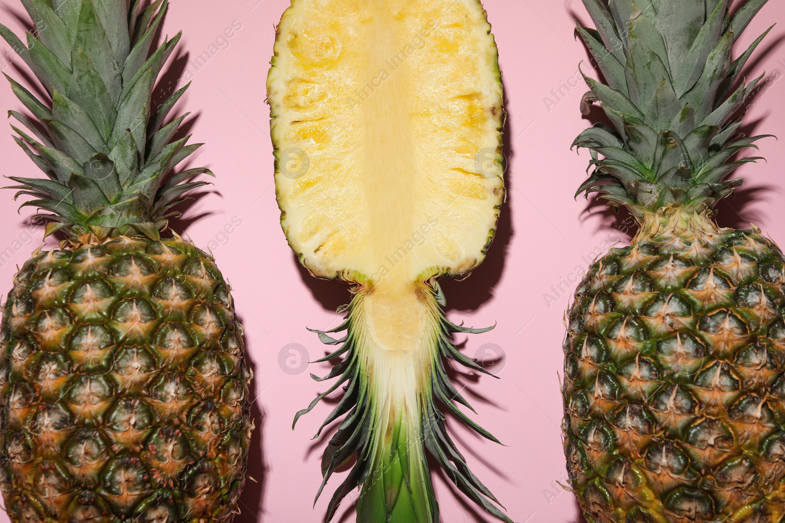 Photo of Whole and cut ripe pineapples on pale pink background, flat lay