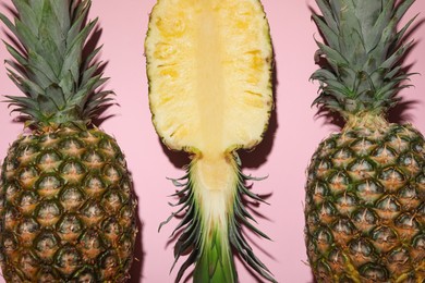 Whole and cut ripe pineapples on pale pink background, flat lay