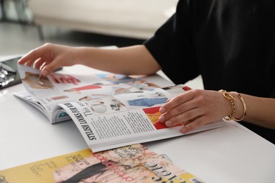 Photo of Woman reading fashion magazine at white table indoors, closeup