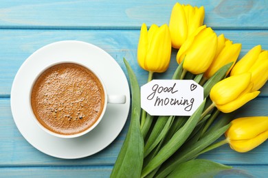 Photo of Cup of aromatic coffee, beautiful yellow tulips and Good Morning note on light blue wooden table, flat lay