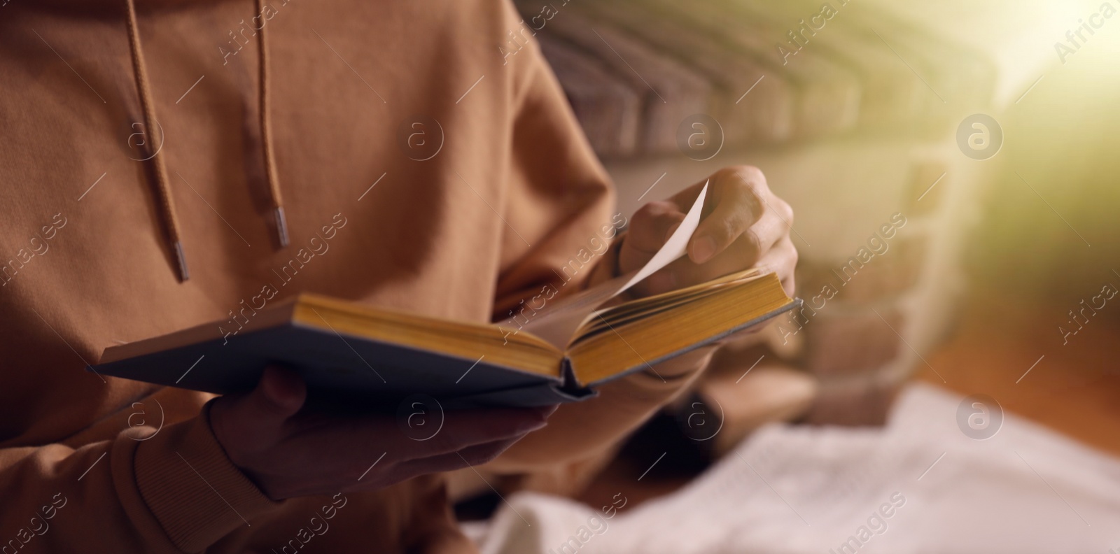 Image of Man reading book near fireplace at home, closeup. Banner design