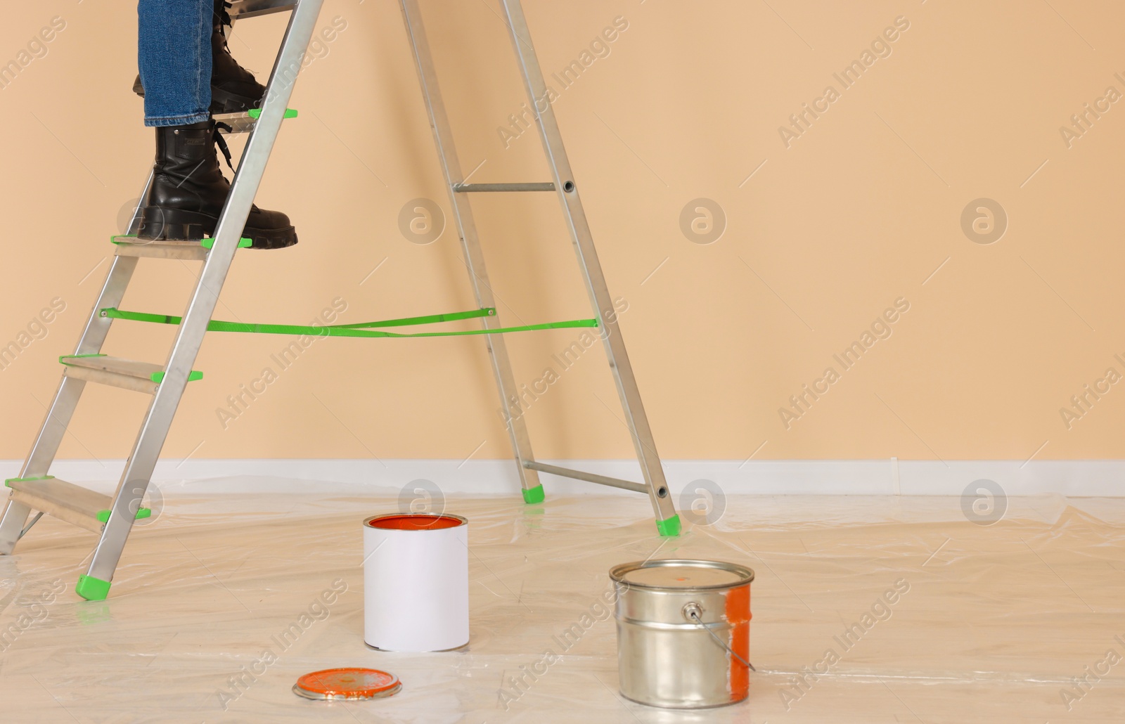 Photo of Woman climbing up metal stepladder near wall indoors, closeup. Room renovation