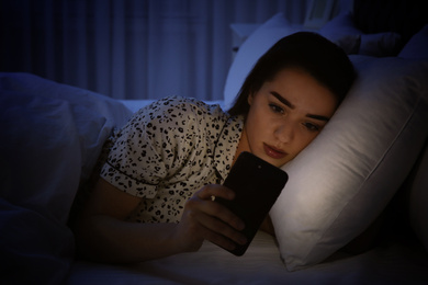 Young woman addicted to smartphone in bed at night