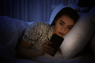 Photo of Young woman addicted to smartphone in bed at night