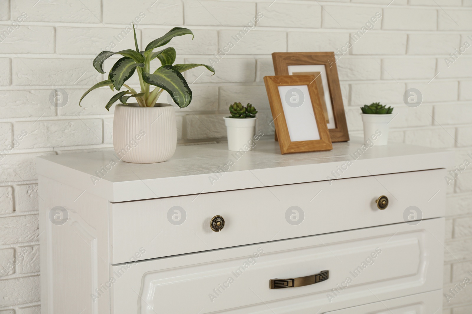 Photo of Modern chest of drawers with decor near white brick wall