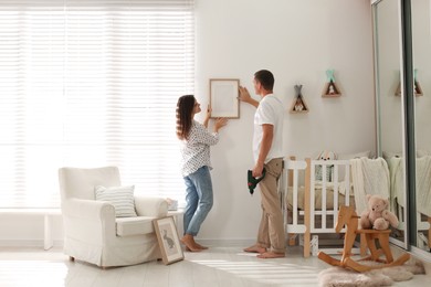 Photo of Happy couple decorating baby room with pictures together. Interior design