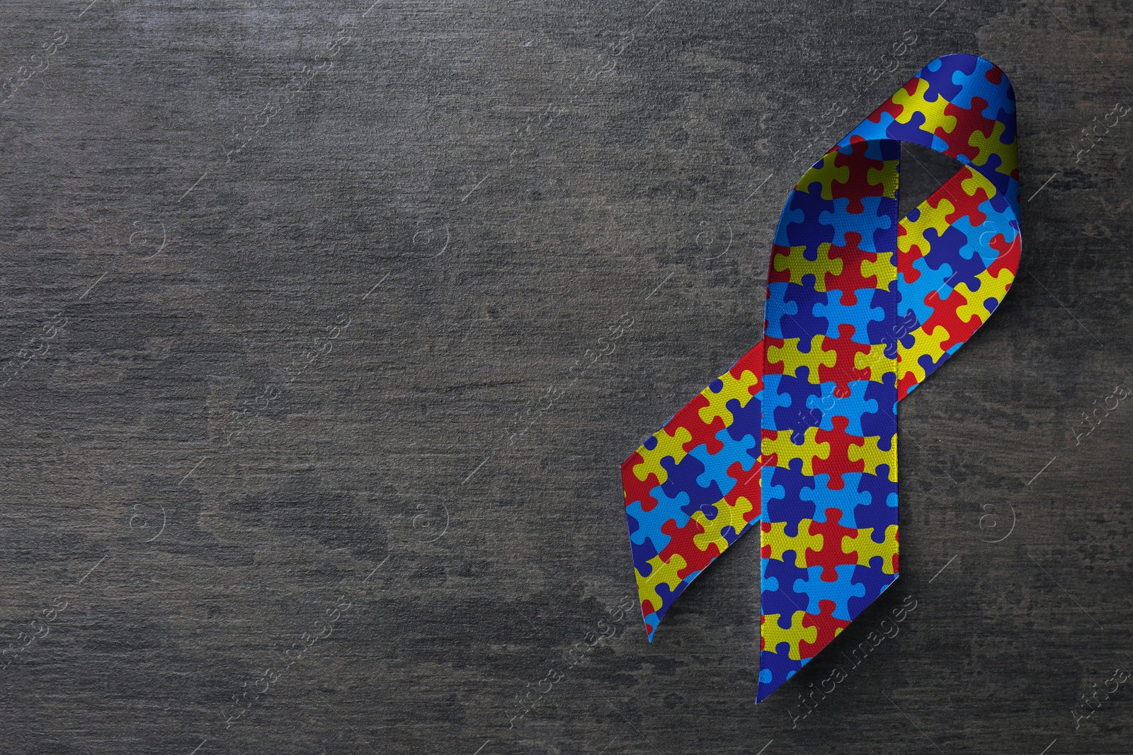 Image of World Autism Awareness Day. Colorful puzzle ribbon on grey stone background, top view with space for text