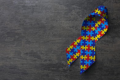 Image of World Autism Awareness Day. Colorful puzzle ribbon on grey stone background, top view with space for text