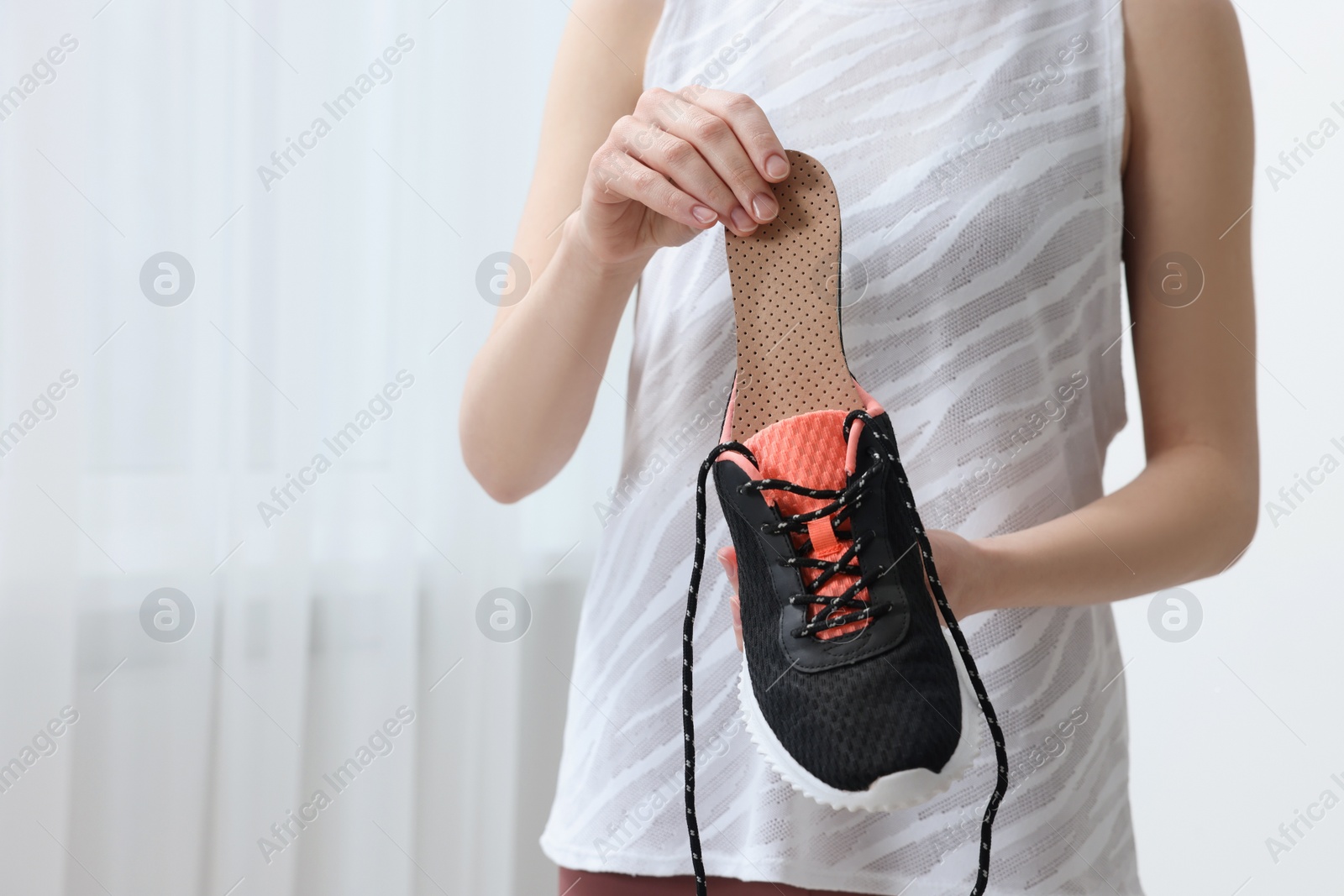 Photo of Woman putting orthopedic insole into shoe indoors, closeup and space for text. Foot care