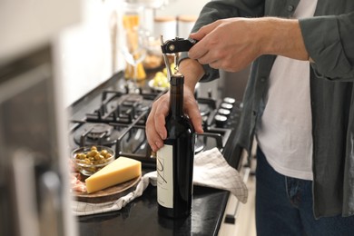 Man opening wine bottle with corkscrew at black countertop indoors, closeup