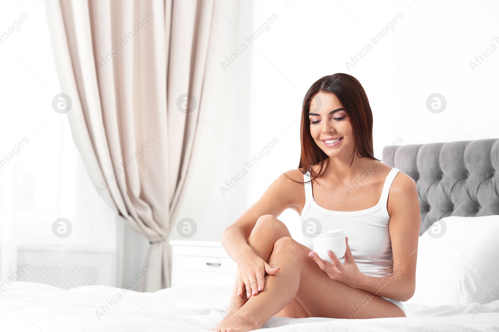 Photo of Young woman with jar of cream in bedroom, space for text. Beauty and body care