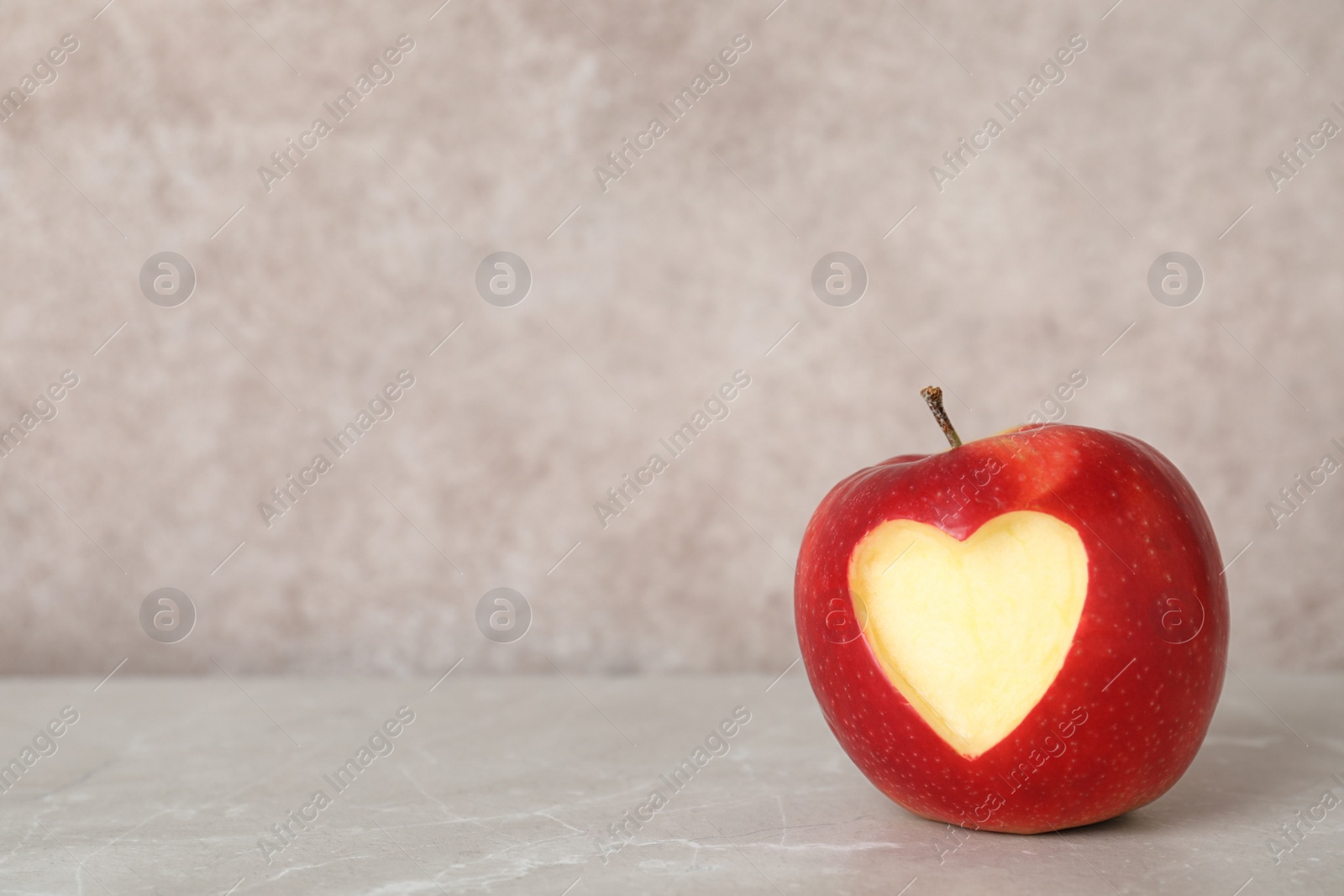 Photo of Red apple with carved heart on table against grey background. Space for text