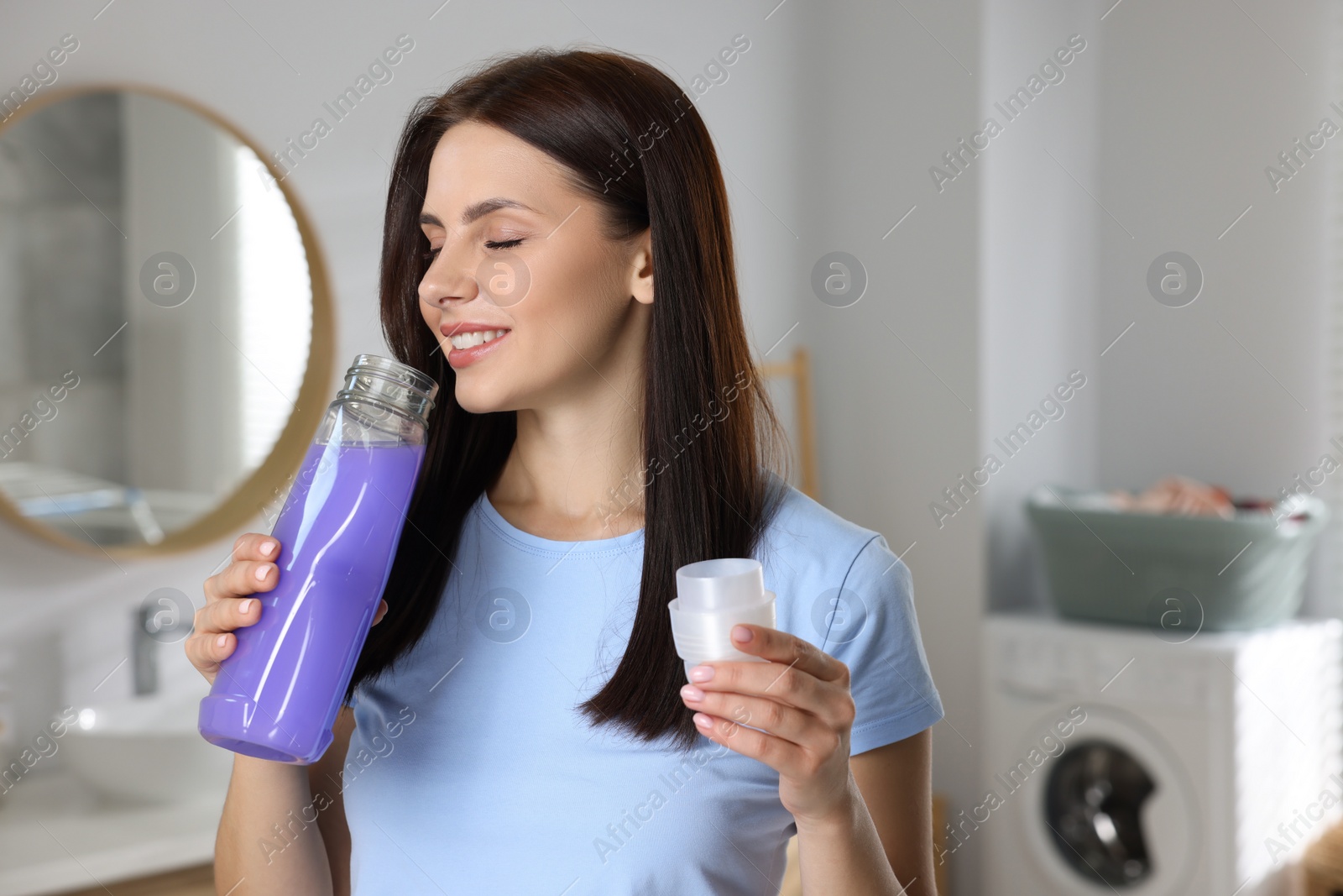 Photo of Woman smelling fabric softener in bathroom, space for text