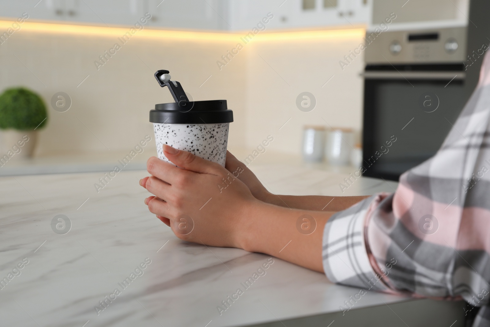 Photo of Woman with reusable coffee cup at table indoors, closeup