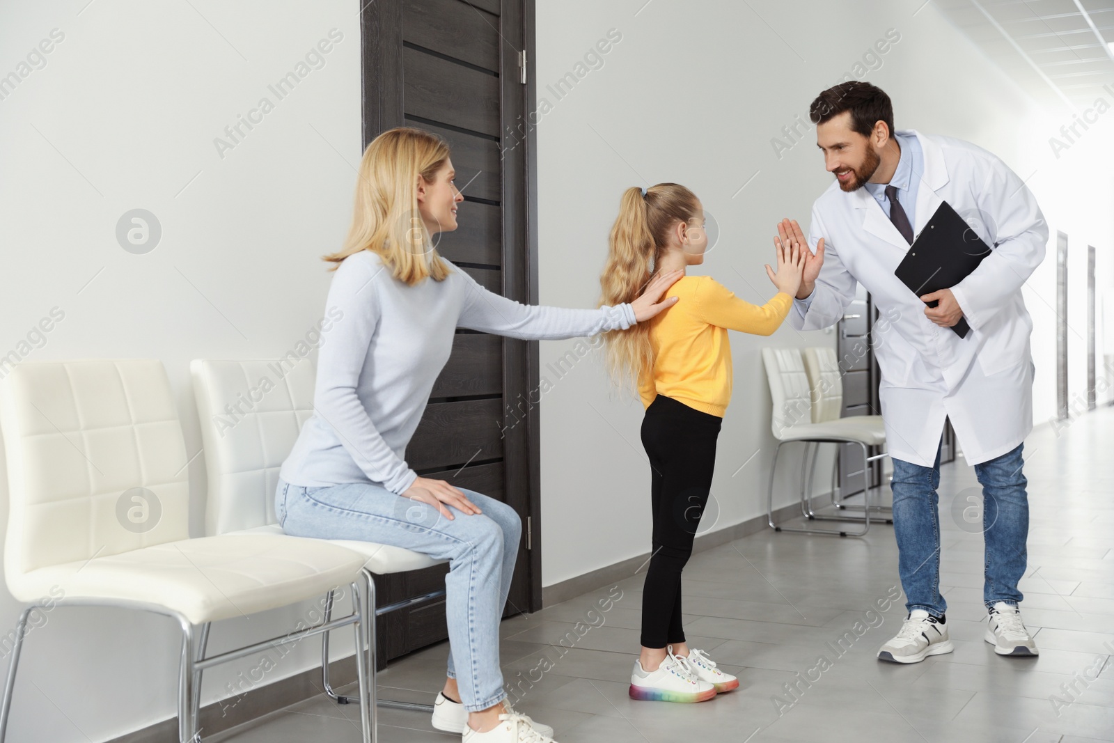 Photo of Happy mother and daughter having appointment with doctor. Pediatrician and patient giving high five in clinic