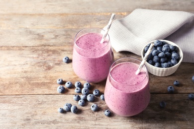 Tasty blueberry smoothie in glasses and berries on wooden table