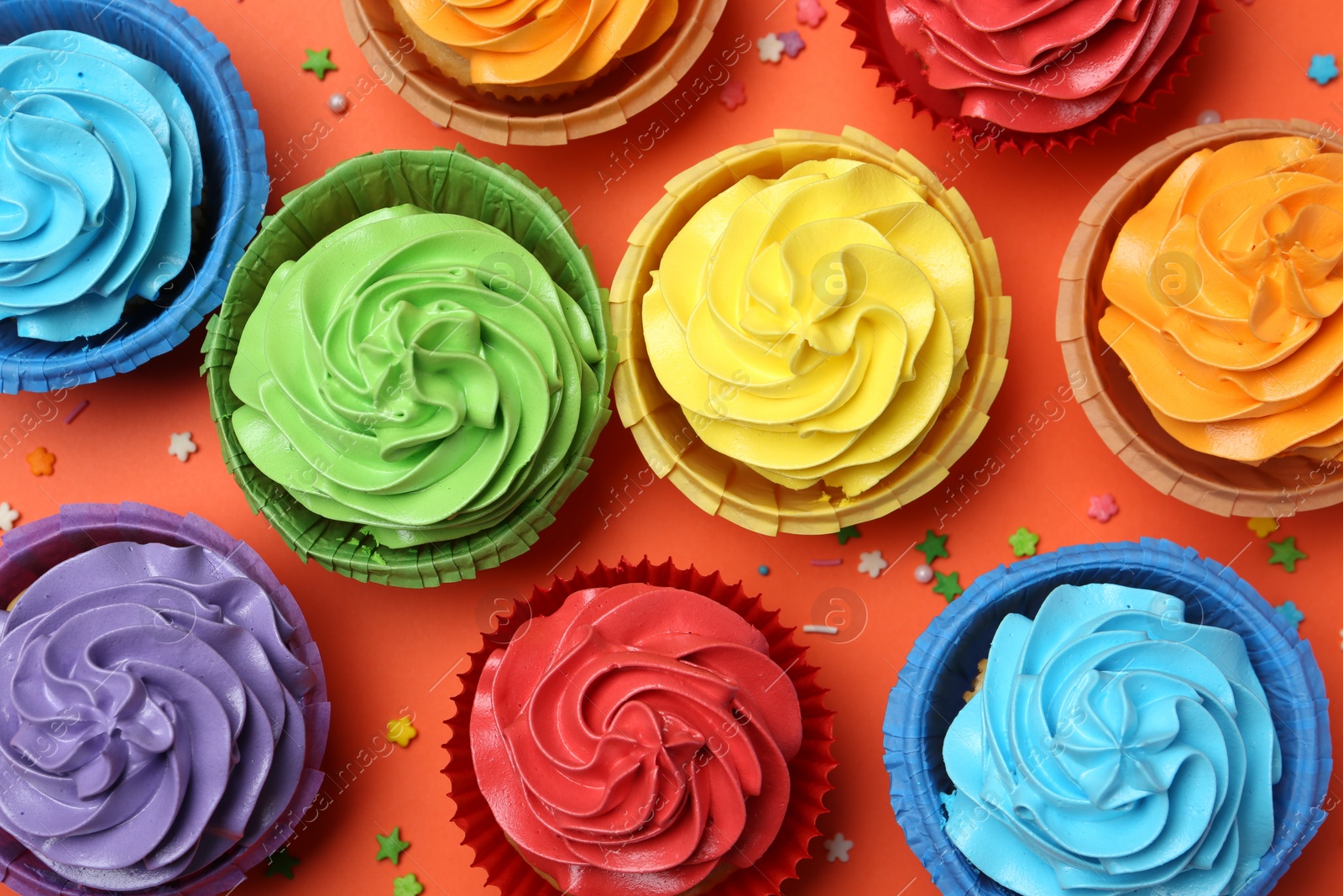 Photo of Delicious bright cupcakes and sprinkles on coral background, flat lay