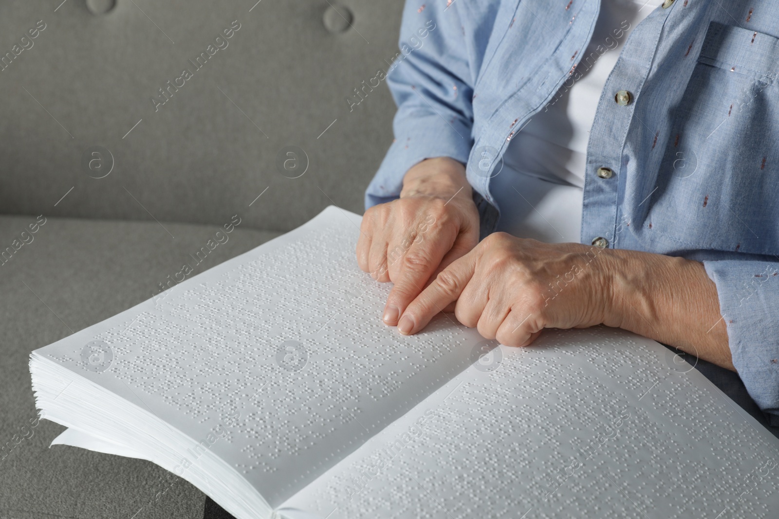 Photo of Blind senior person reading book written in Braille on sofa, closeup