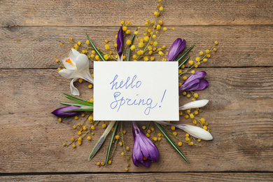 Photo of Card with words HELLO SPRING and fresh flowers on wooden table, flat lay