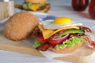 Photo of Fresh juicy bacon burger on white wooden table