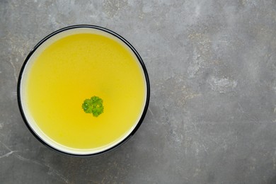 Delicious chicken bouillon with parsley on grey table, top view. Space for text