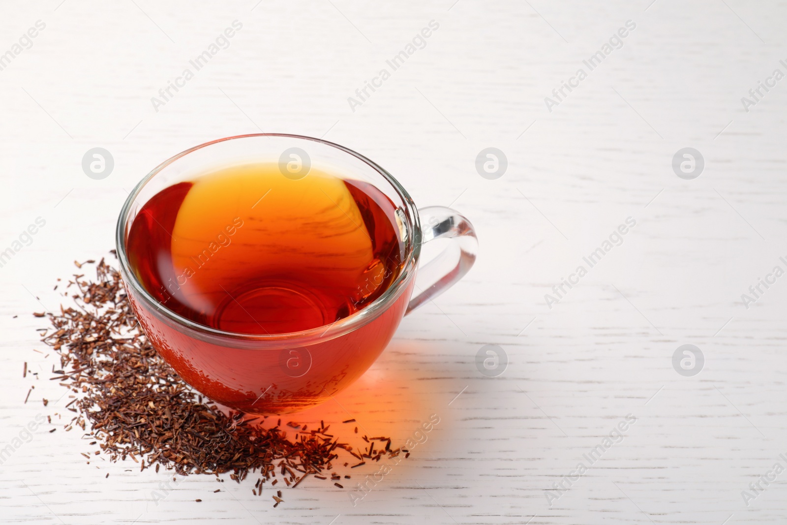 Photo of Freshly brewed rooibos tea and scattered dry leaves on white wooden table. Space for text