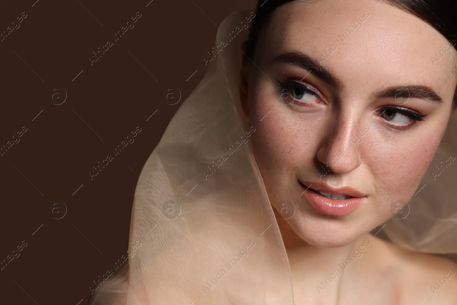Photo of Fashionable portrait of beautiful woman with fake freckles on brown background, closeup. Space for text