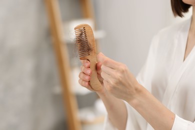 Photo of Woman taking her lost hair from comb at home, closeup. Alopecia problem