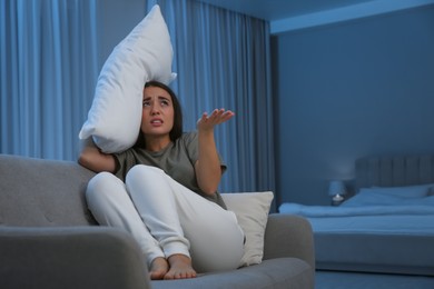 Photo of Young woman with pillow suffering from noisy neighbours in living room at night
