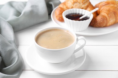 Fresh croissants, jam and coffee on white wooden table. Tasty breakfast