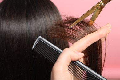 Photo of Hairdresser cutting client's hair with scissors on pink background, closeup