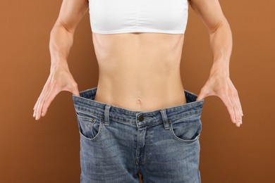 Photo of Slim woman wearing big jeans on brown background, closeup. Weight loss