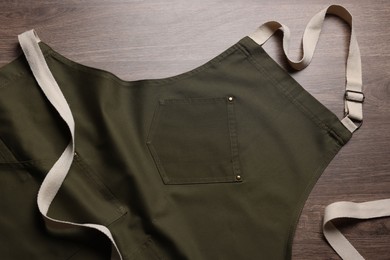 Photo of Stylish dark olive apron on wooden table, top view. Mockup for design