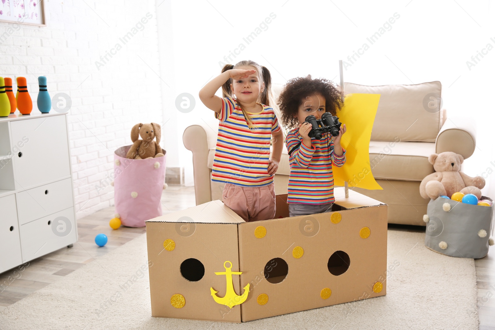 Photo of Cute little children playing with cardboard ship and binoculars at home