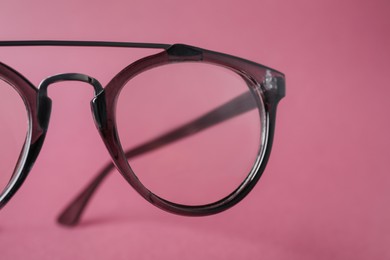 Stylish pair of glasses with plastic frame on pink background, closeup