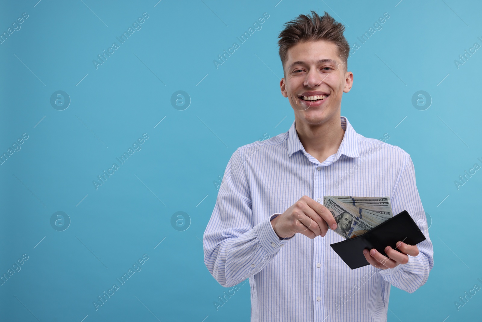 Photo of Happy man putting dollar banknotes into wallet on light blue background. Space for text