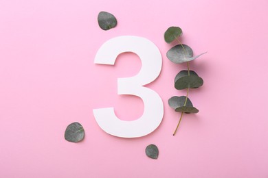 Paper number 3 and eucalyptus leaves on pink background, flat lay