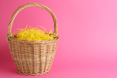 Photo of Easter basket with yellow paper filler on pink background, space for text