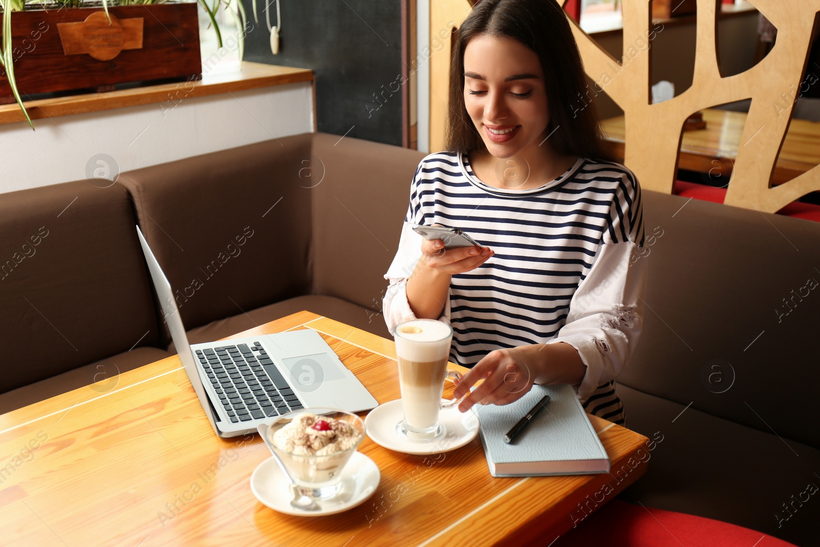 Photo of Young blogger taking picture of dessert and latte at table in office