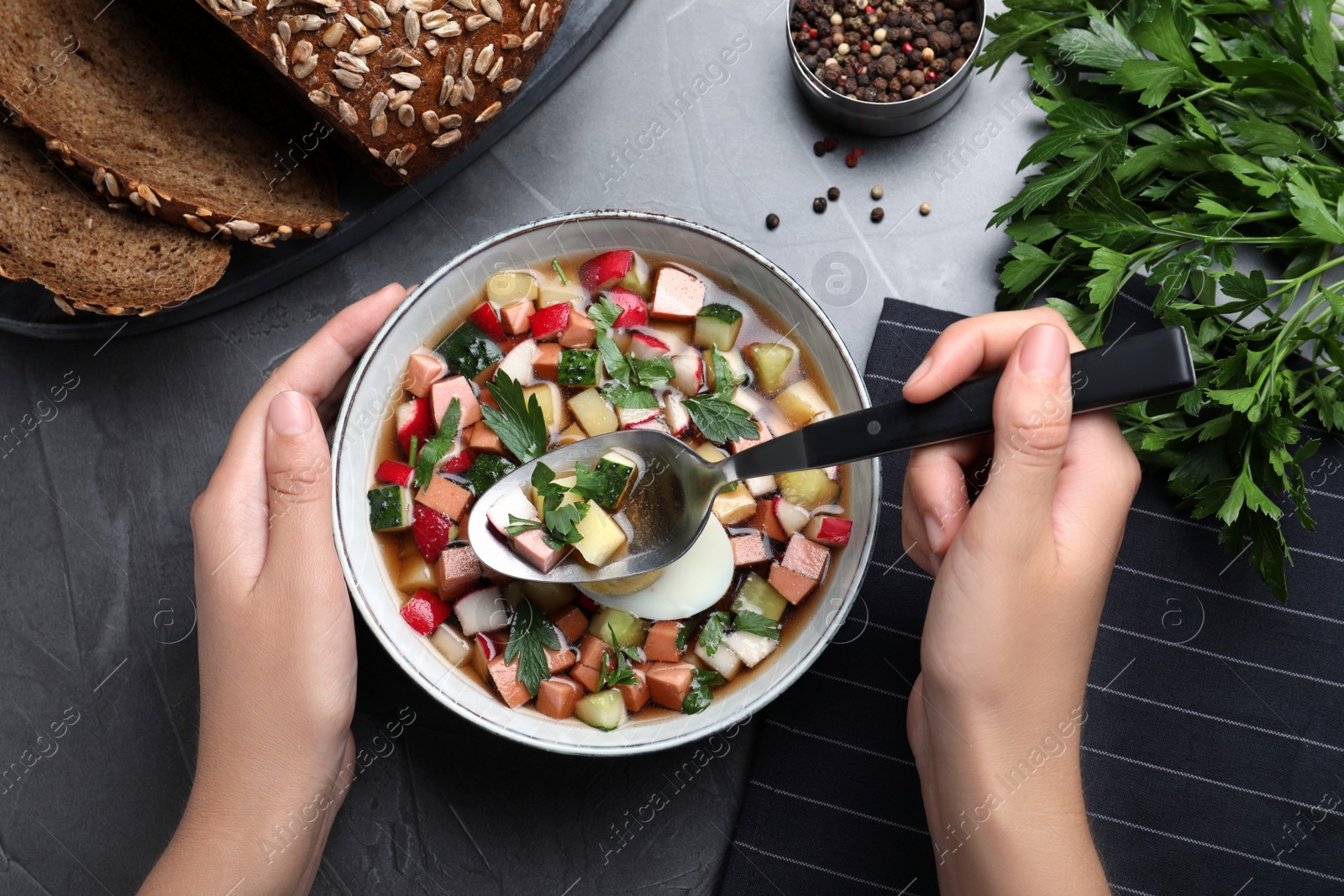 Photo of Woman eating delicious cold okroshka with kvass at grey table, top view. Traditional Russian summer soup